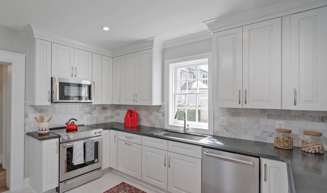Bright white kitchen with stainless steel appliances, gray countertops, and a window over the sink