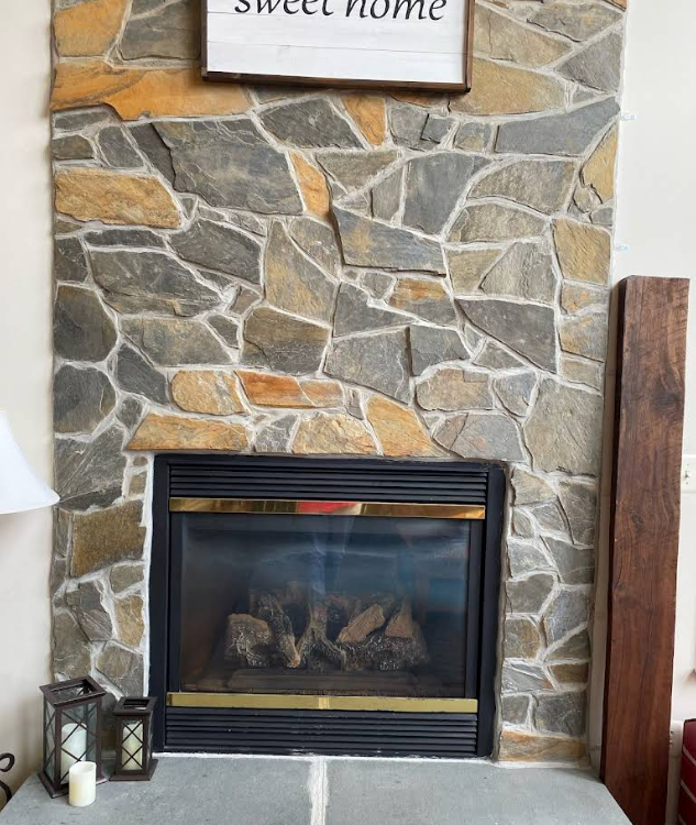 Stone fireplace with black insert, candles, and a “Sweet Home” sign above it