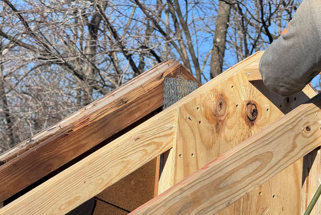 Close-up of a wooden roof frame with rafters against a blue sky and bare trees