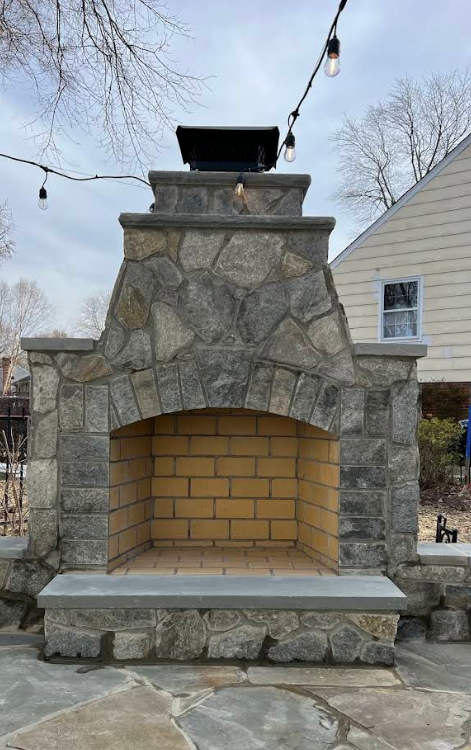 Stone outdoor fireplace with arched brick firebox and string lights overhead in a backyard