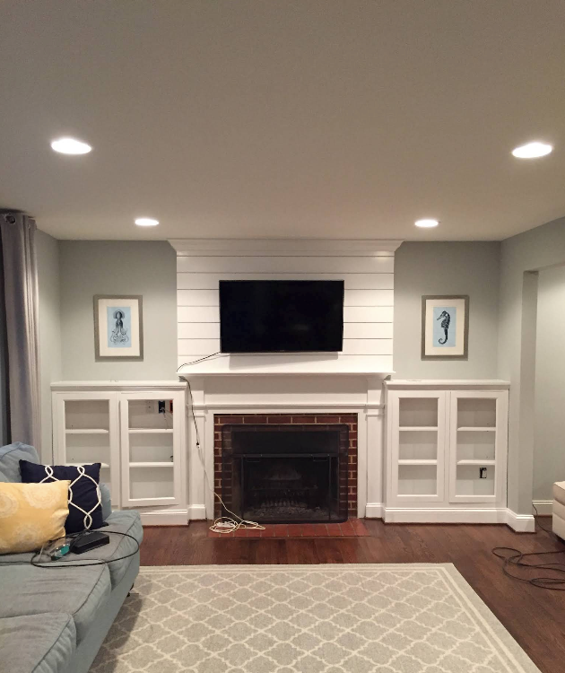 Living room with fireplace, wall-mounted TV, built-ins, and a light rug on hardwood floors.