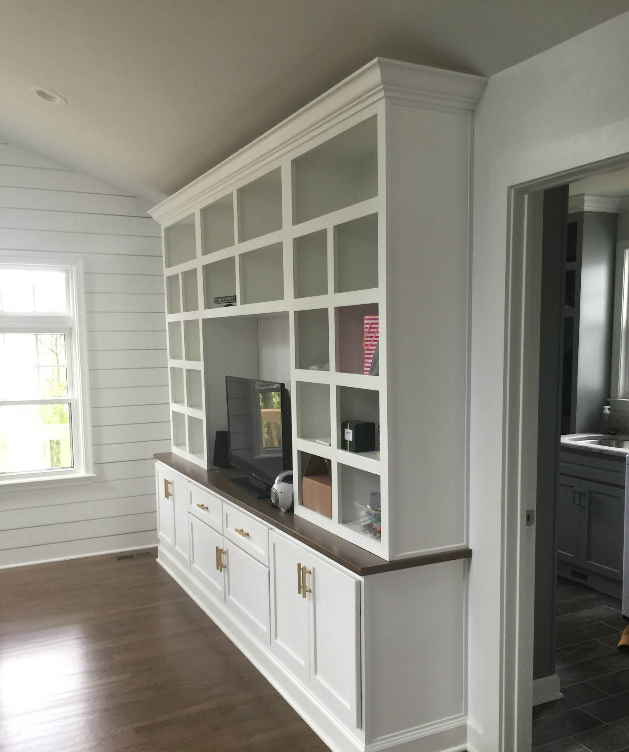 Built-in white shelving and cabinets in a bright room with a window and wood floor.