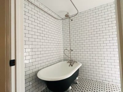 Small bathroom with a black-and-white clawfoot tub, white subway tile walls, and a patterned tile floor.