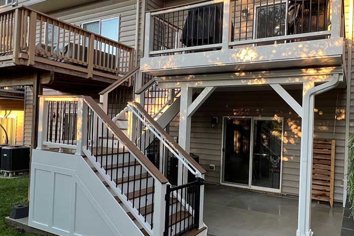 Outdoor apartment patio with wooden stairs, railing, and sliding glass doors under a balcony