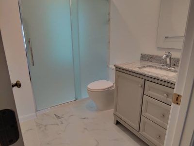 Modern bathroom with frosted glass shower, toilet, and white vanity with marble countertop.