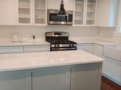 Bright white kitchen with marble island, stainless gas stove, hanging hood, and white cabinets