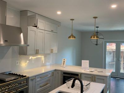 Bright modern kitchen with white cabinets, light blue walls, pendant lights, and a black stove.
