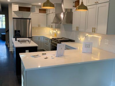 Modern white kitchen with island, pendant lights, stainless steel appliances, and dark flooring