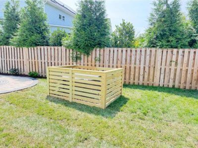 Backyard with a wooden raised planter box on grass near a fence and trees