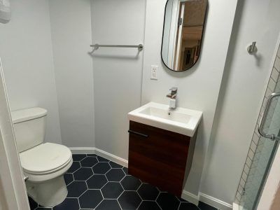 Small bathroom with toilet, vanity sink, mirror, and dark hexagon tile floor.