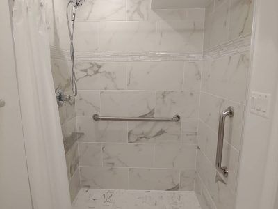Accessible white-tiled shower with grab bars and built-in shelf, viewed from the doorway