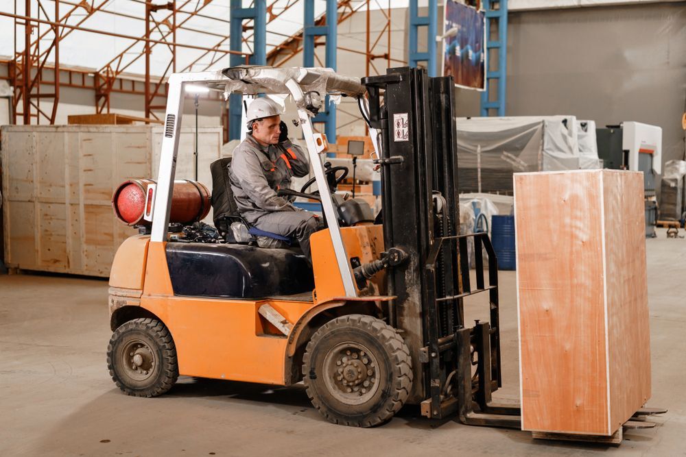 Orange Forklift Lifting a Large Wrapped Pallet in a Warehouse — Forklift Repairs & Spares In Svensson Heights, QLD