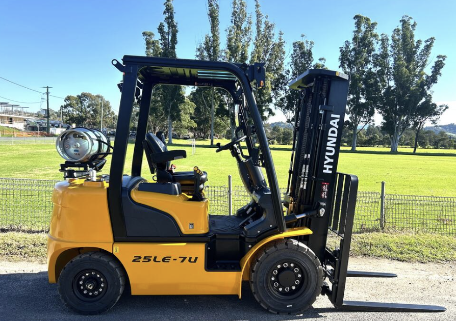Yellow Hyundai forklift parked outdoors on grass with trees in the background