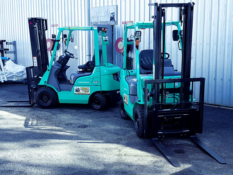 Two Green Forklifts Parked a Metal Warehouse — Forklift Repairs & Spares In Hervey Bay, QLD