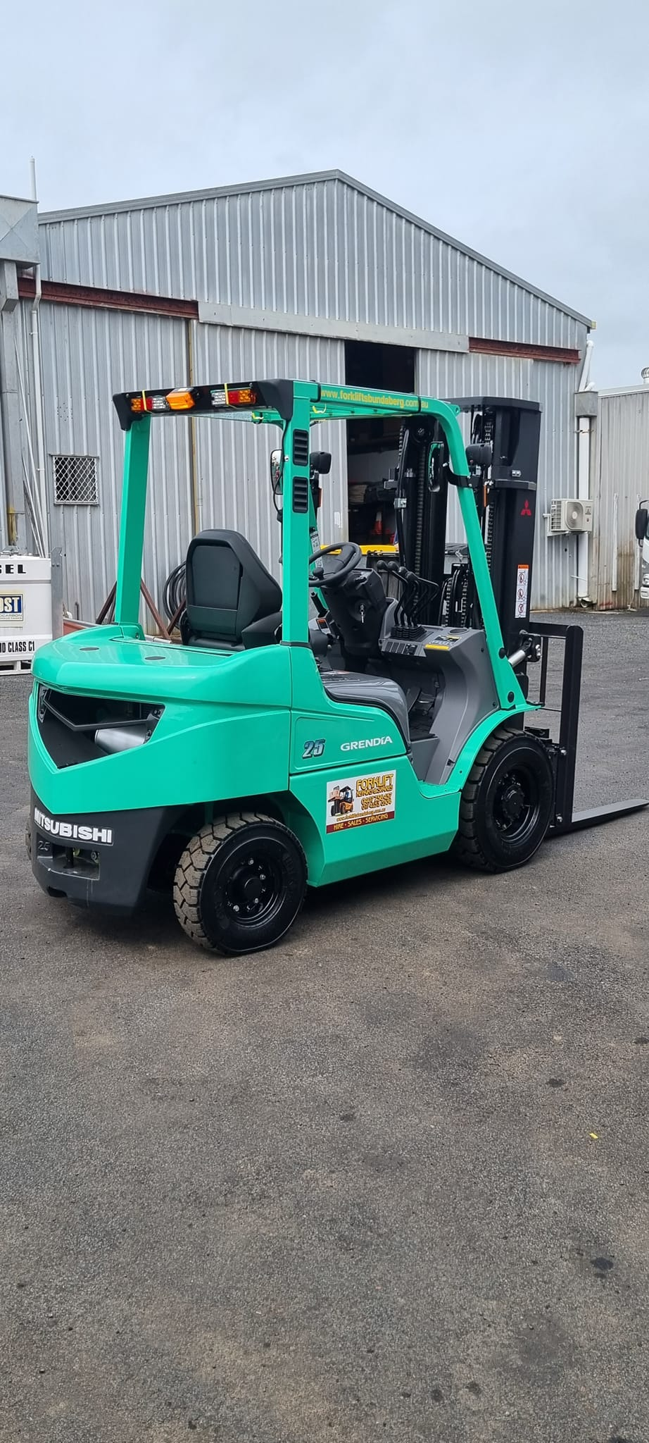 Turquoise Forklift Parked on Gravel Outside a Metal Warehouse Building — Forklift Repairs & Spares In Svensson Heights, QLD