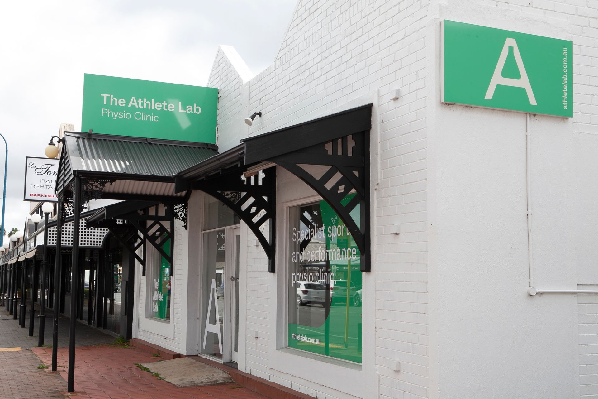 White building with black awnings, green signs for