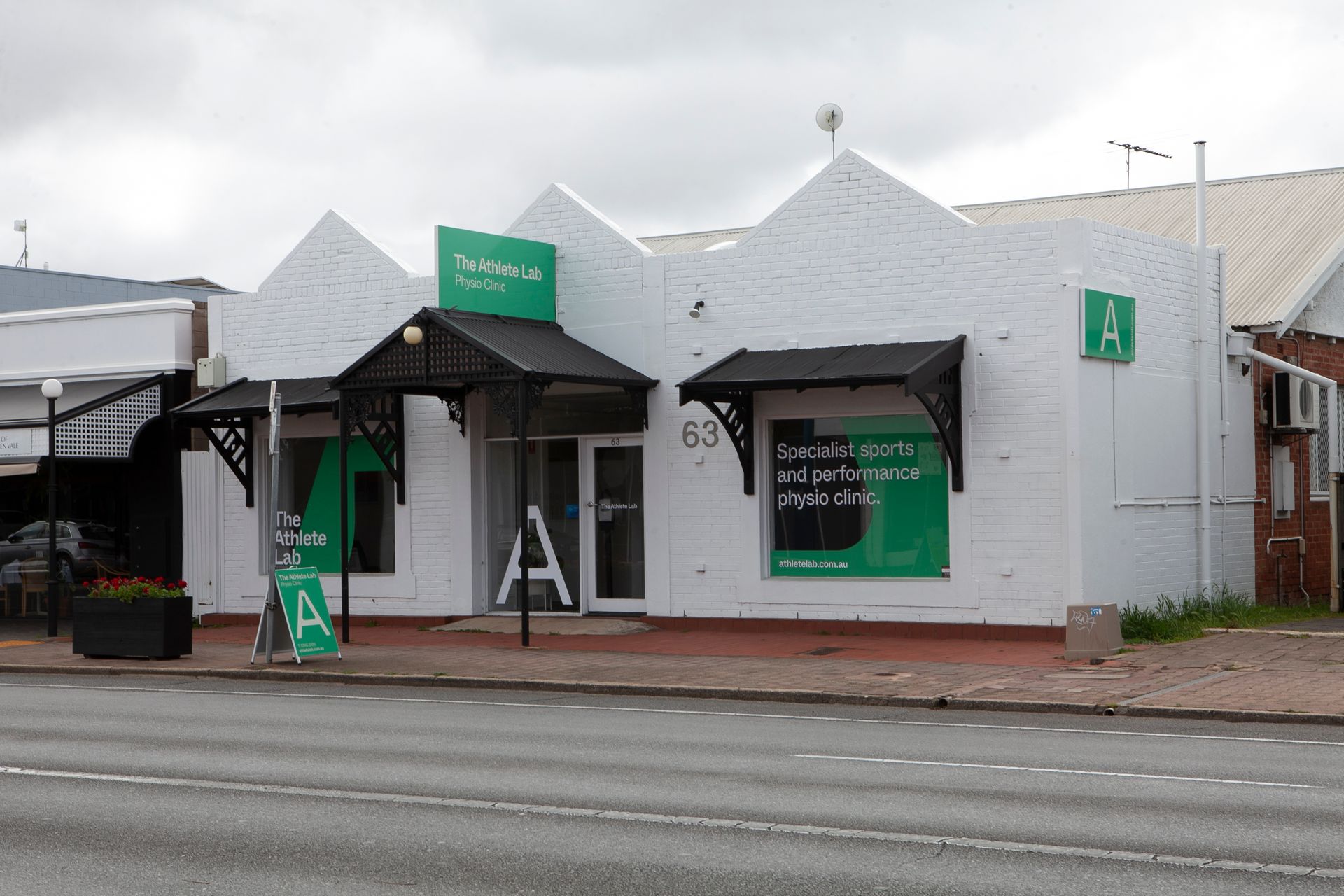 White storefront with green signage; black awnings.