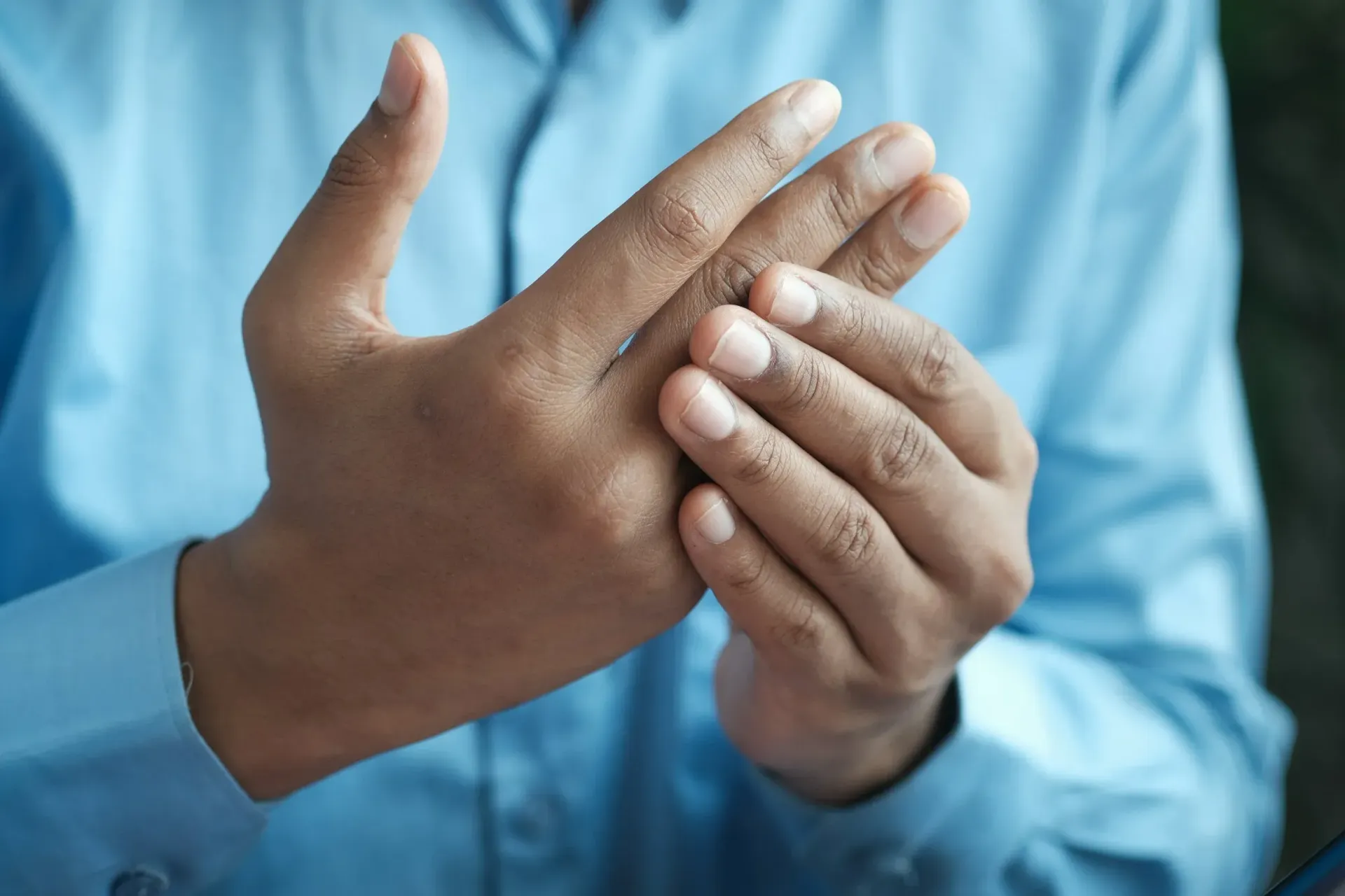 Person in blue shirt holding hand, looking at other hand.