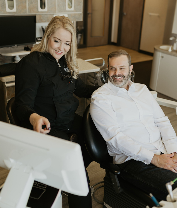 A woman is sitting next to a man in a dental chair looking at a computer screen.