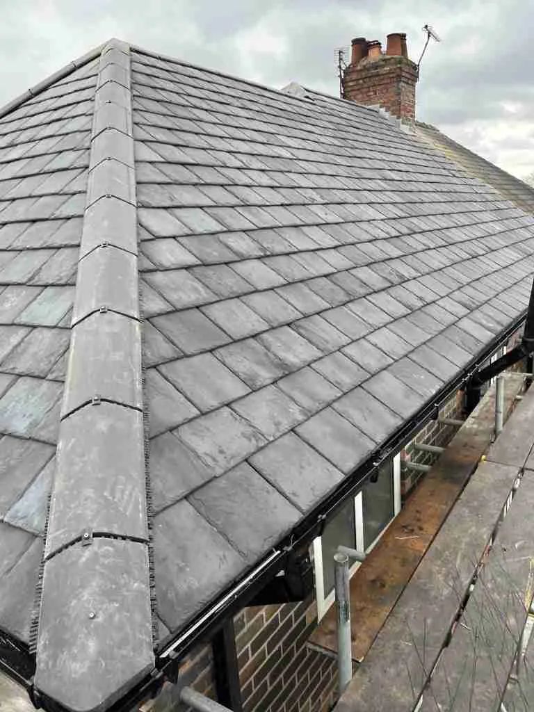 Gray tiled roof of a brick building. Black gutters and scaffolding are visible. Chimney in background.
