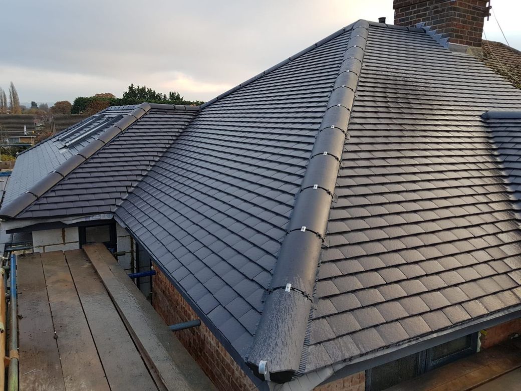 Newly tiled dark gray roof with a chimney and skylights on a house exterior.