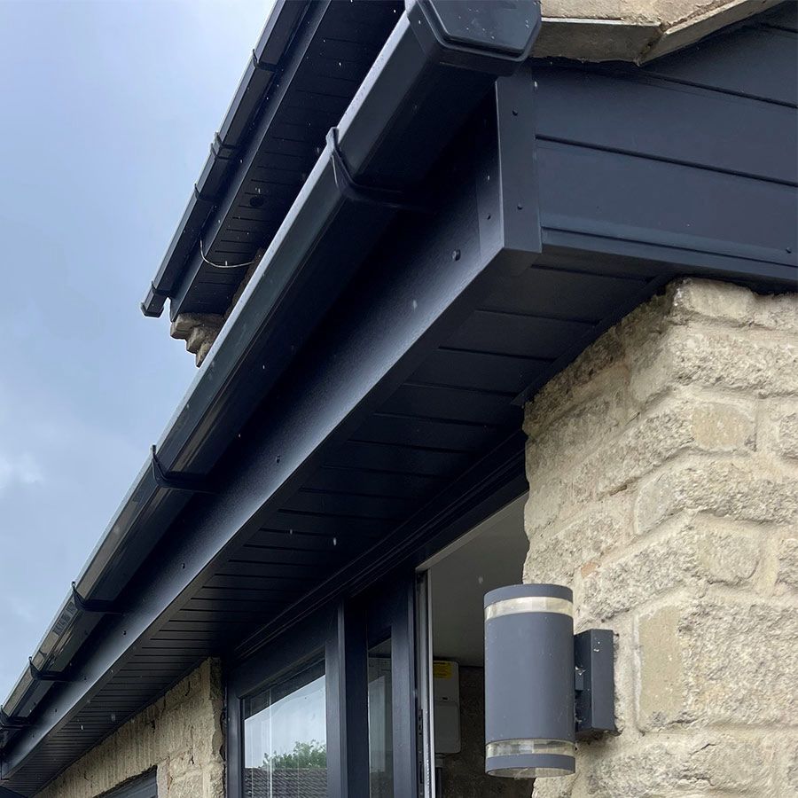 Black rain gutters and trim on a light stone building with a window and outdoor light fixture.