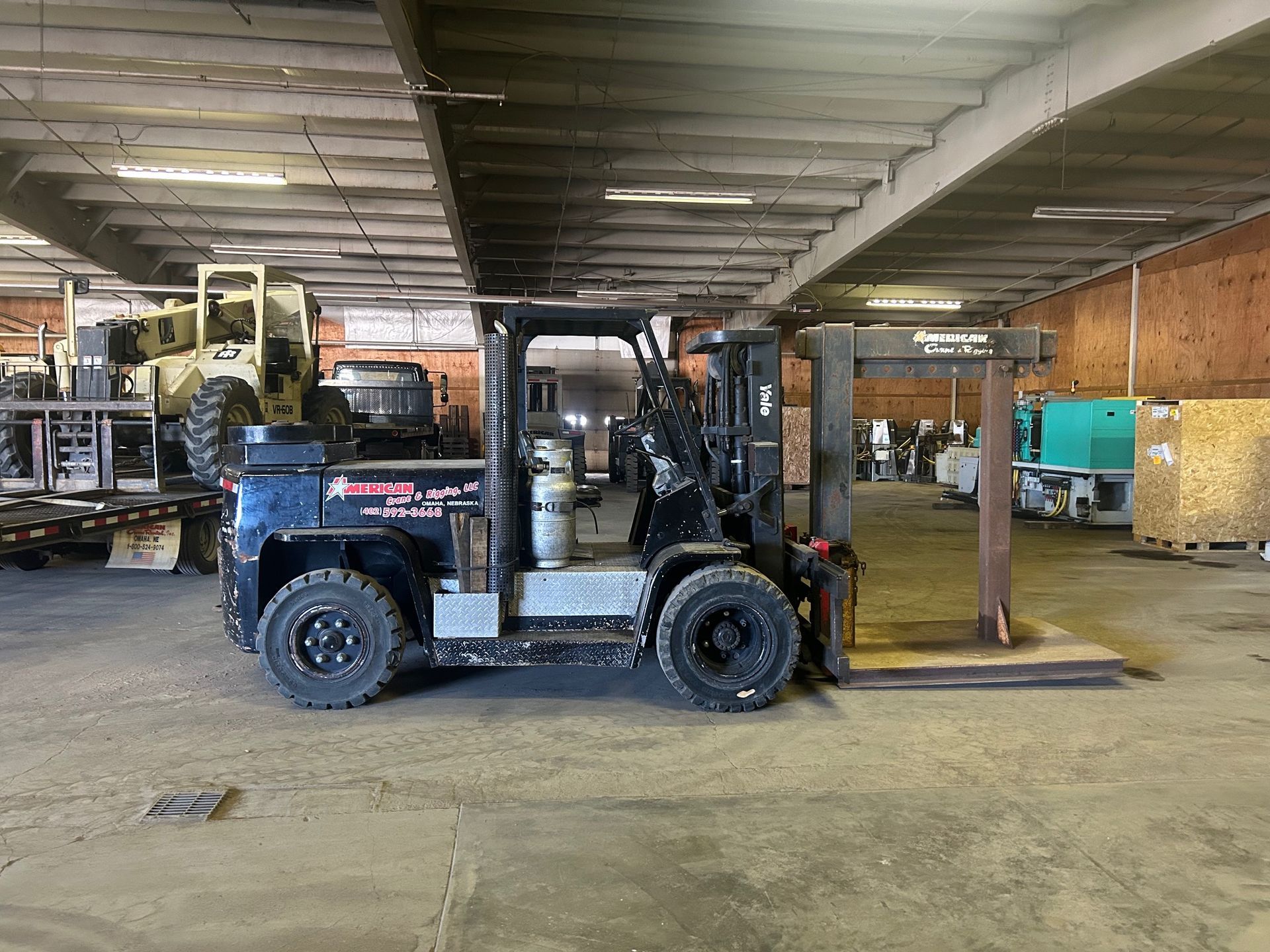Warehouse workers in hard hats review plans near a yellow forklift.