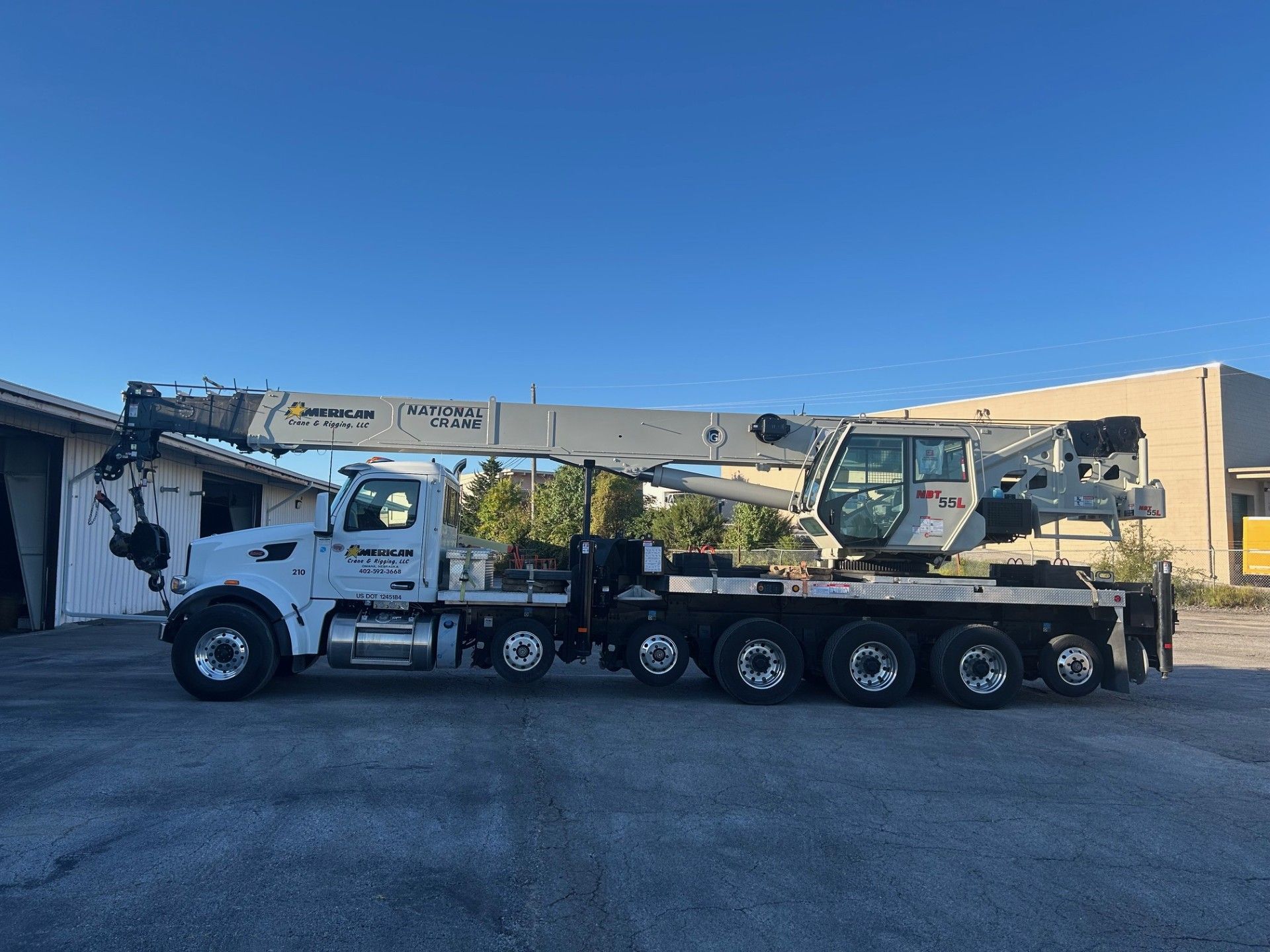 Orange crane on wheels, extending arm, parked on snow, blue sky.