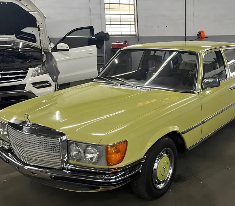 Yellow vintage Mercedes sedan parked indoors in a garage, front-left view