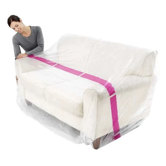 Person securing a white couch in a clear cover with a pink strap wrapping around it