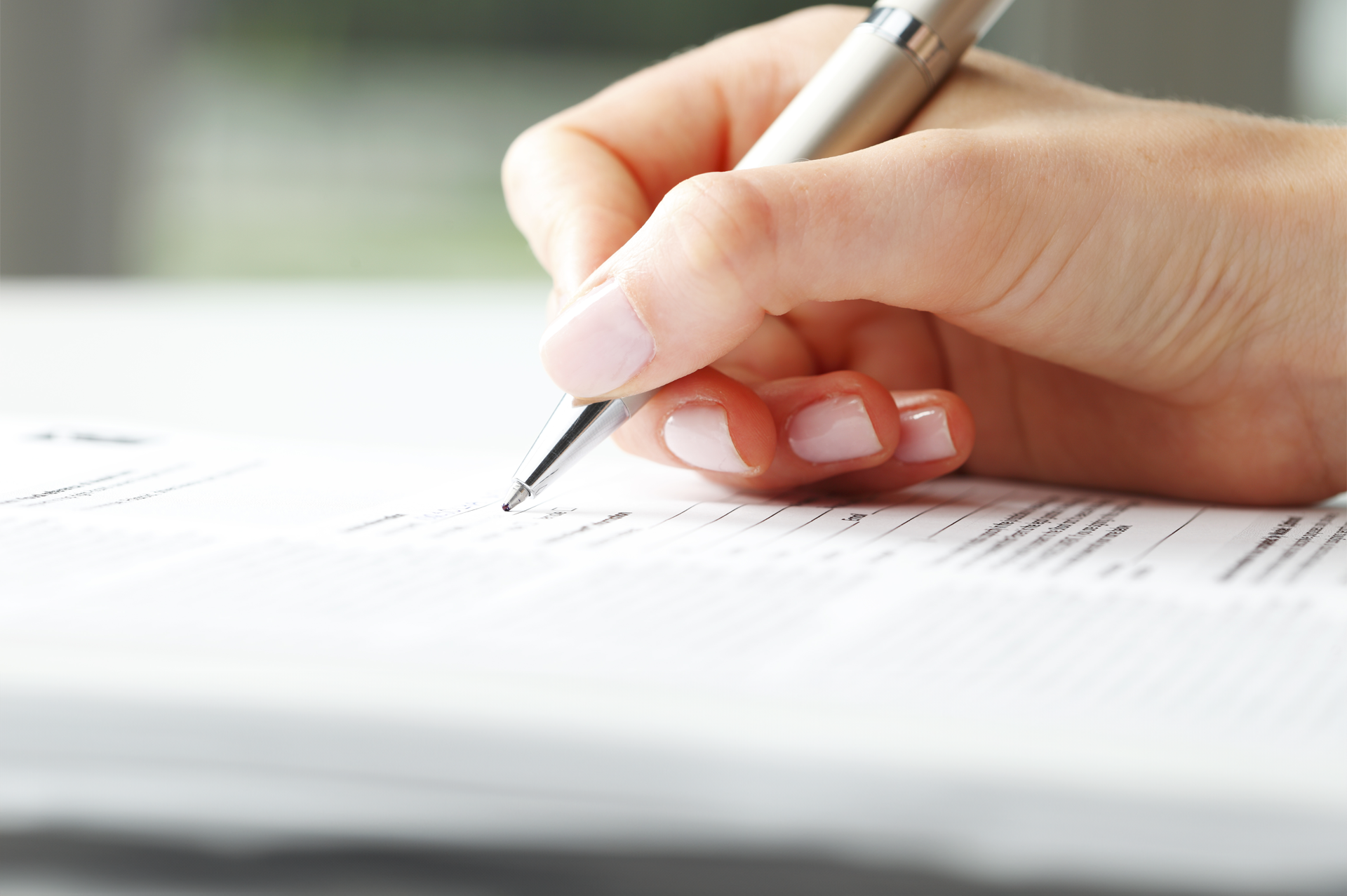Hand holding a pen and signing a document on a white desk