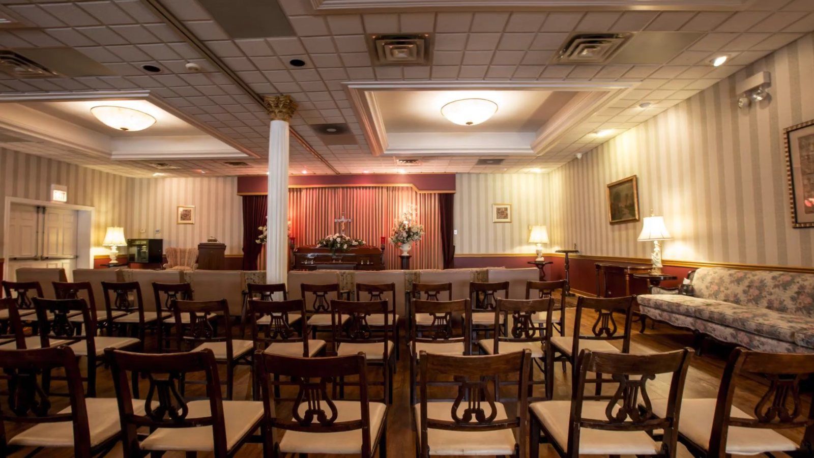 Visitation room at the Caring Cremations funeral home in Chicago, with rows of chairs facing flower arrangements and red drapes