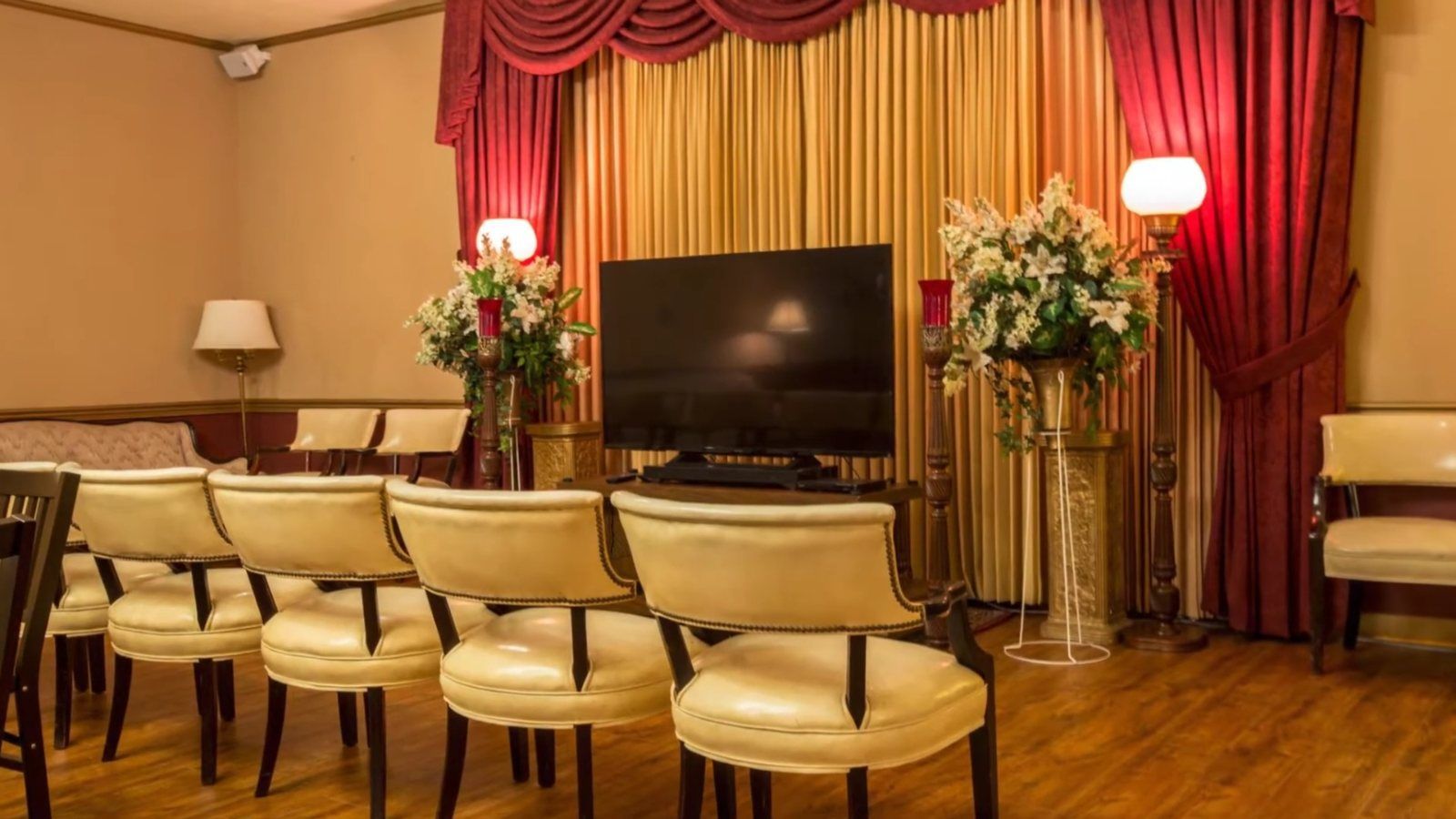 Front of a visitation room with flower arrangements, lamps and a screen for a tribute video