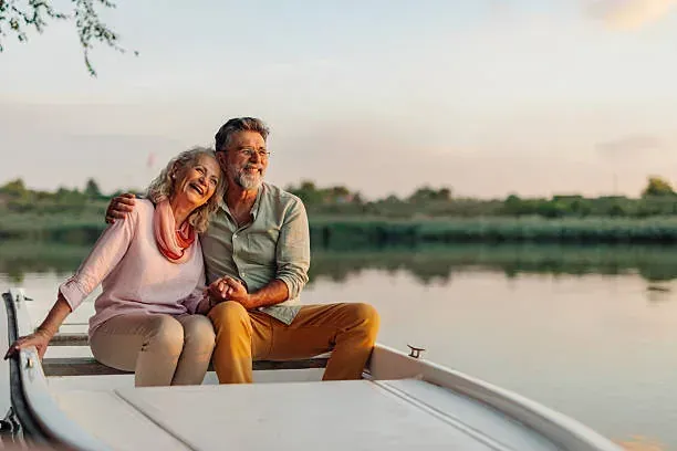 Smiling older couple sitting close together in a boat on a calm lake at sunset