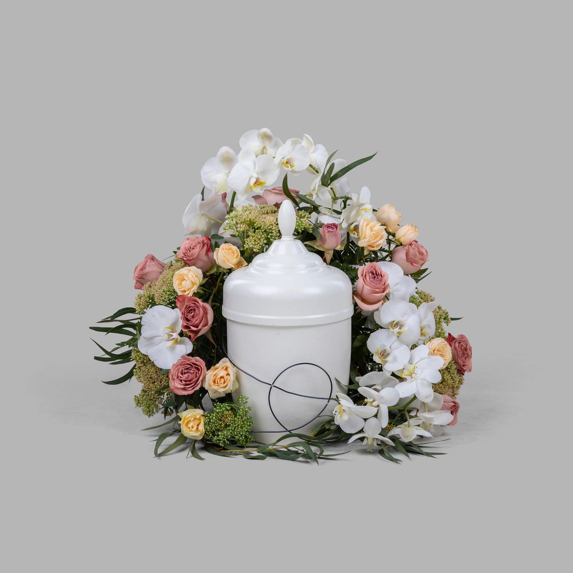 White urn surrounded by pastel pink, peach, and white flowers on a gray background