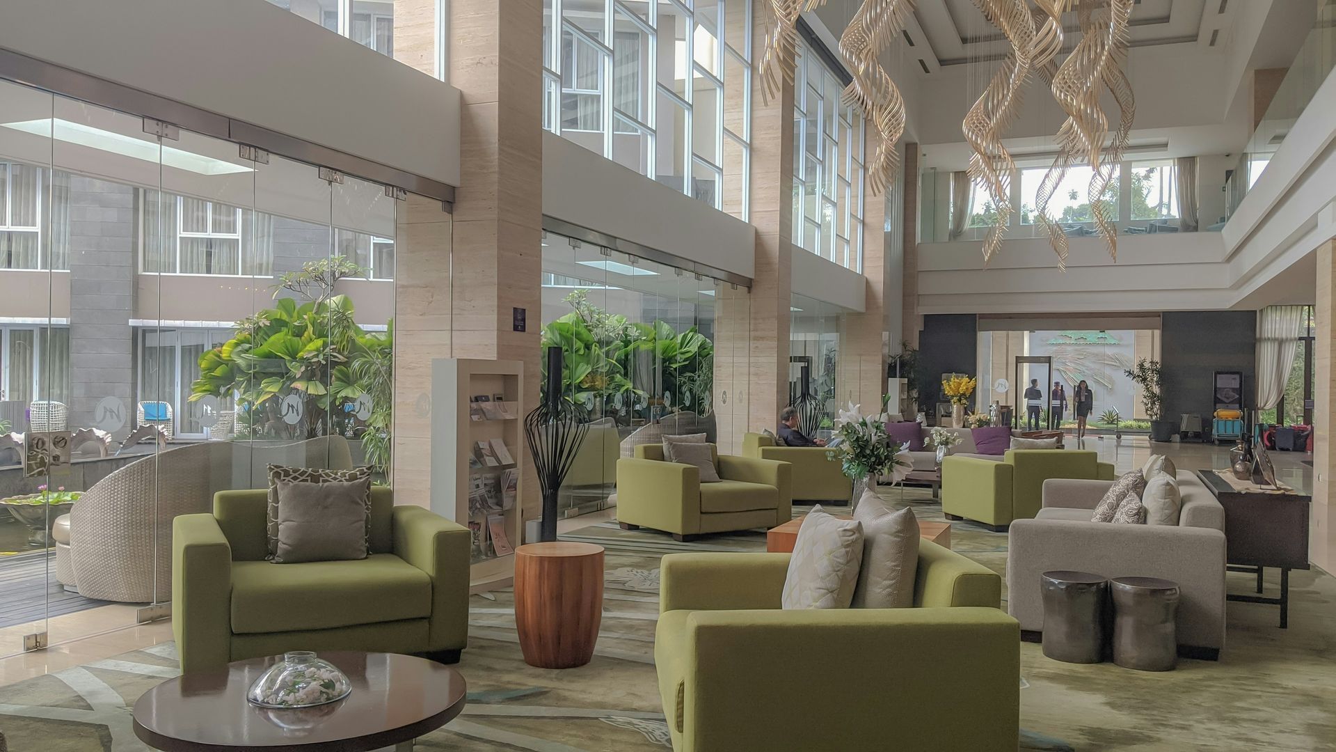 Modern hotel lobby with green armchairs, lounge seating, large windows, and hanging chandeliers