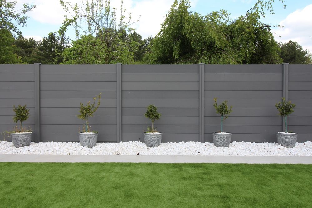 A fence with potted plants and white gravel in front of it.