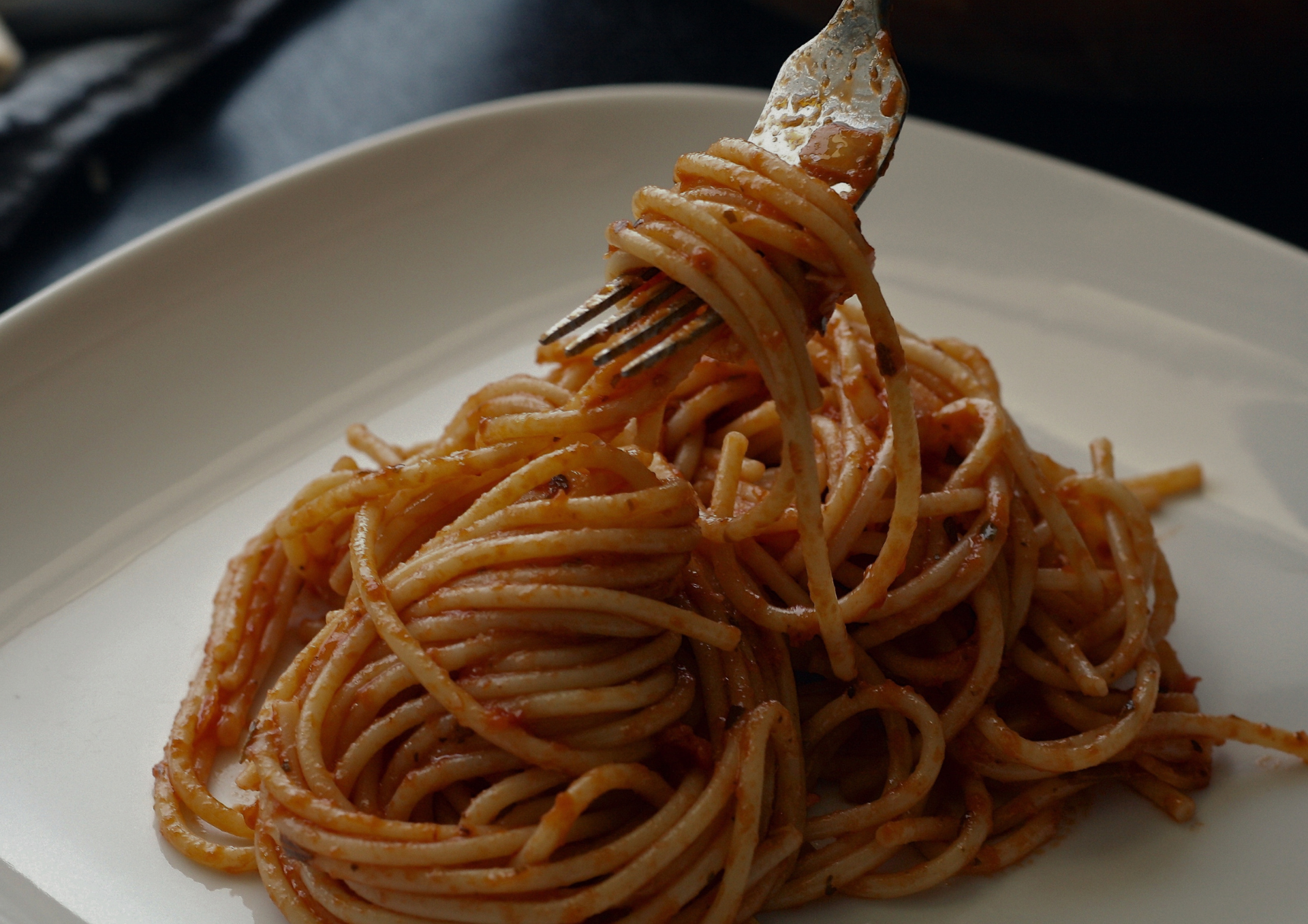 Des spaghettis enroulés en forme de fourchette sur une assiette blanche, nappés de sauce tomate.