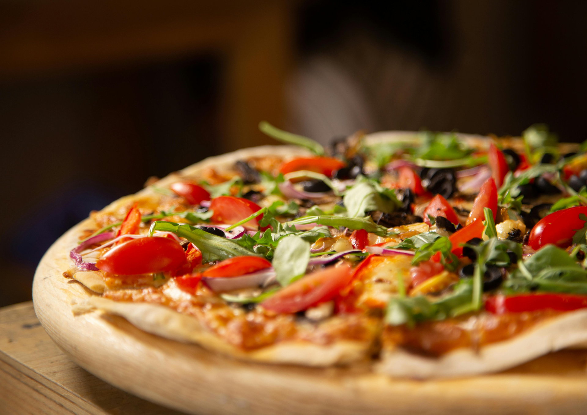Pizza aux légumes frais sur une planche en bois, garnie de tomates, de verdure et d'herbes aromatiques.