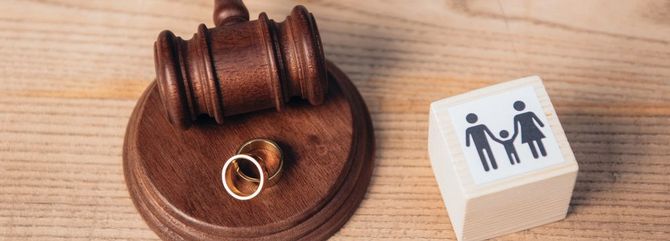 Un martelletto da giudice in legno accanto a fedi nuziali e un piccolo blocco con un'icona di famiglia su una scrivania