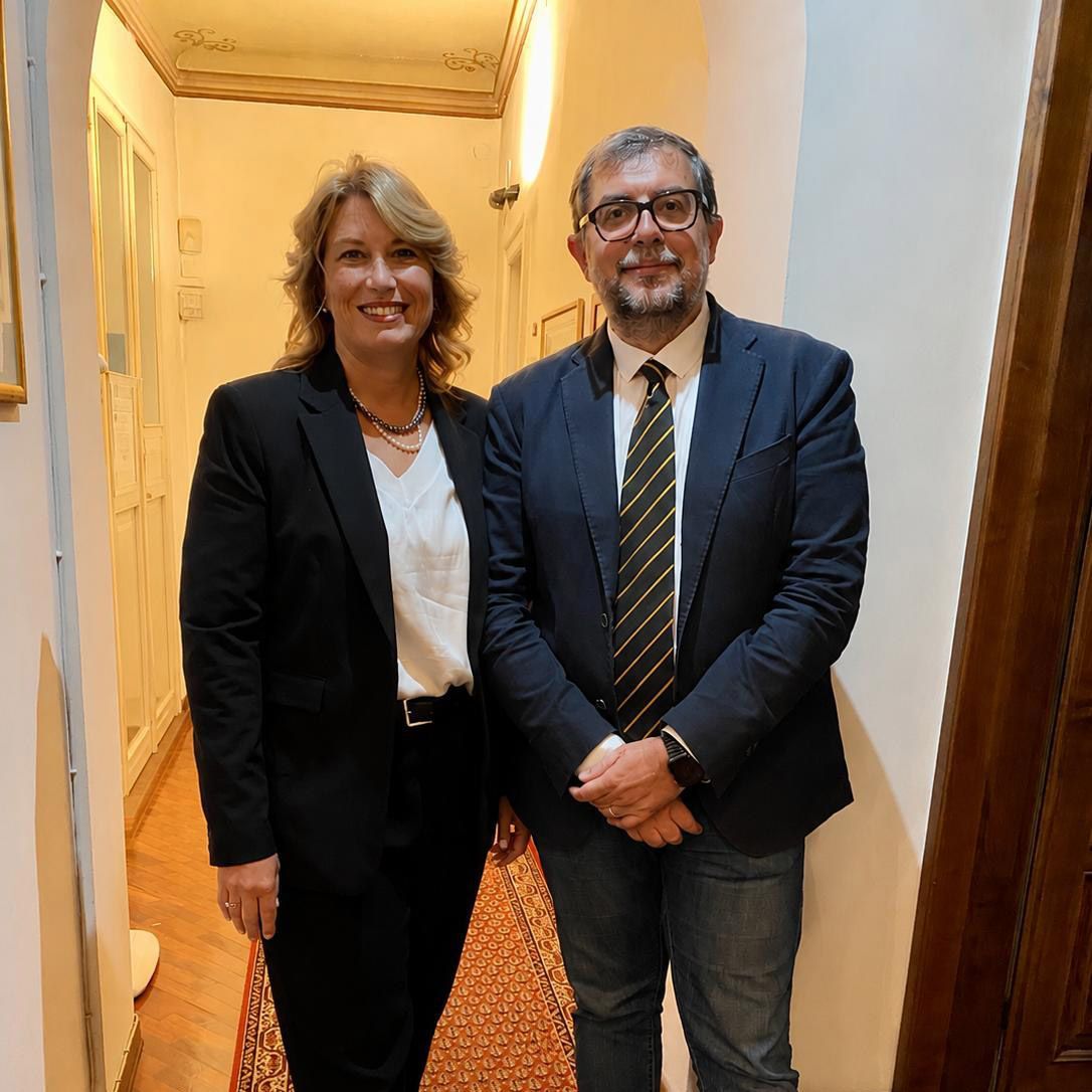 Due persone in abiti da lavoro sorridono in un corridoio illuminato da una luce calda.