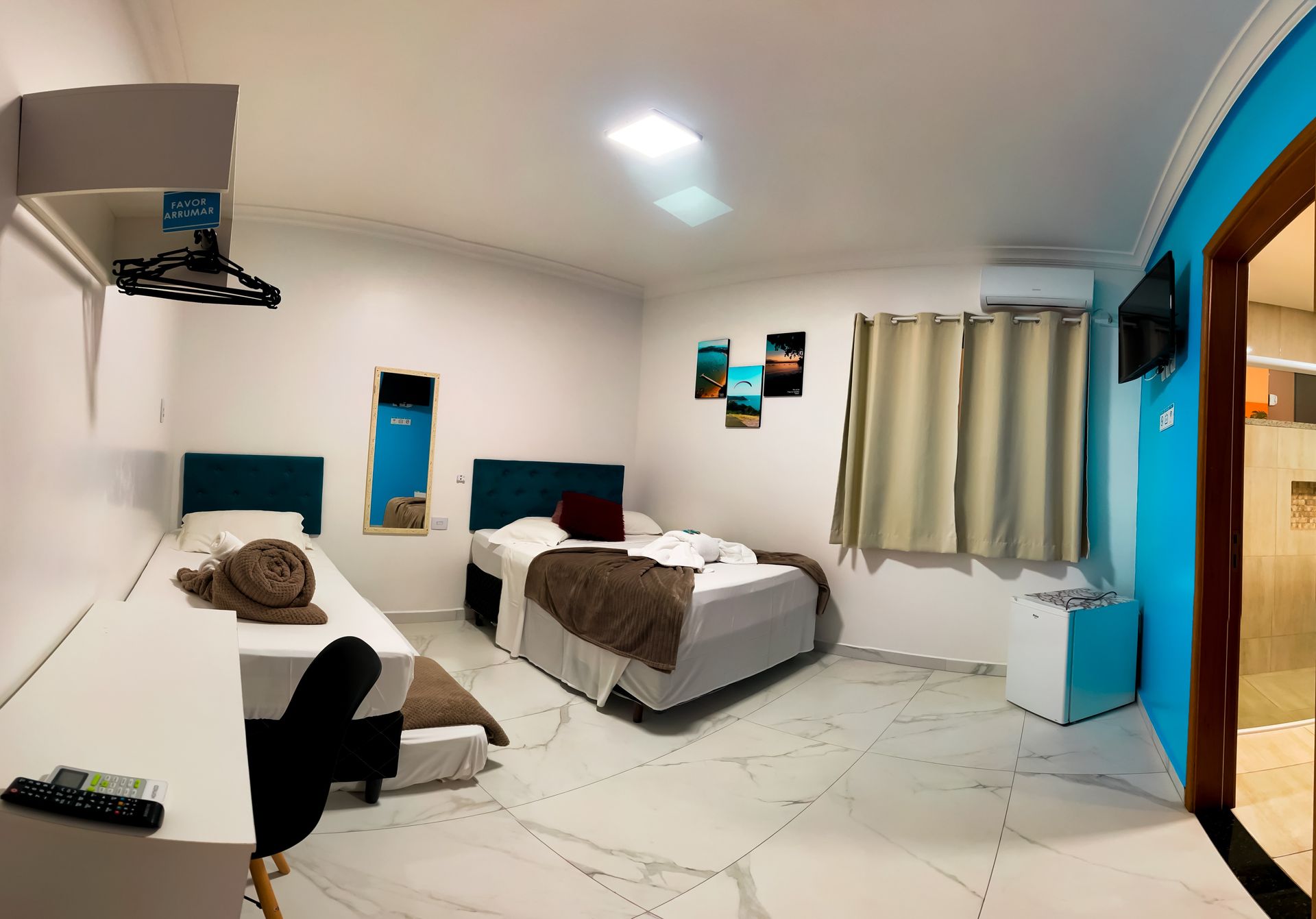Um quarto de hotel com duas camas, paredes brancas, piso de azulejo claro e detalhes em azul nas paredes.