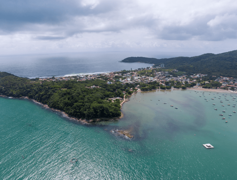 Vista aérea de um promontório verde que separa um mar azul profundo de uma baía turquesa pontilhada de pequenos barcos.