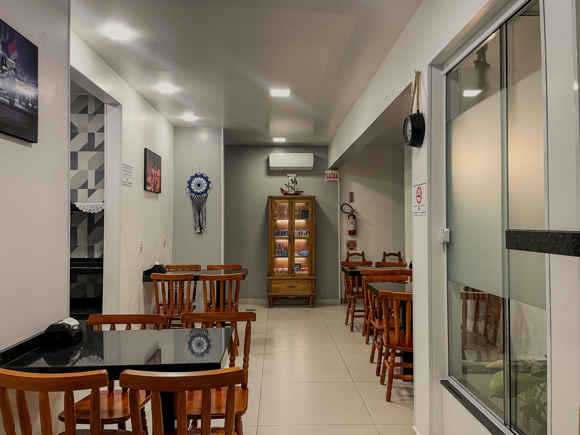Uma sala de jantar com cadeiras e mesas de madeira, um armário de exposição e uma sala com paredes de vidro e iluminação embutida.