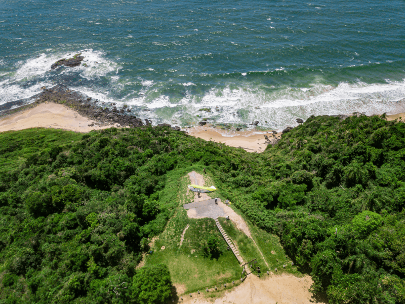 Um parapente decola de um topo de colina gramado com vista para uma costa rochosa e para o oceano.