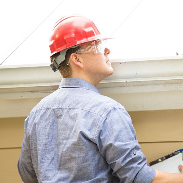 Worker in a red hard hat inspecting a building exterior and holding a clipboard