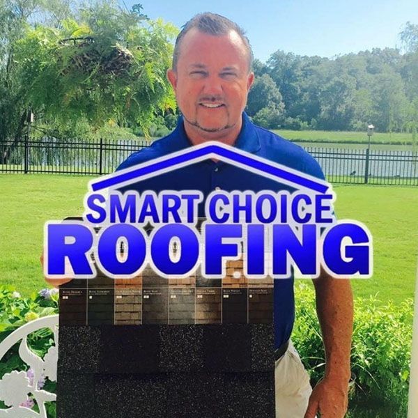 Man standing outdoors behind a Smart Choice Roofing sign on a sunny lawn.