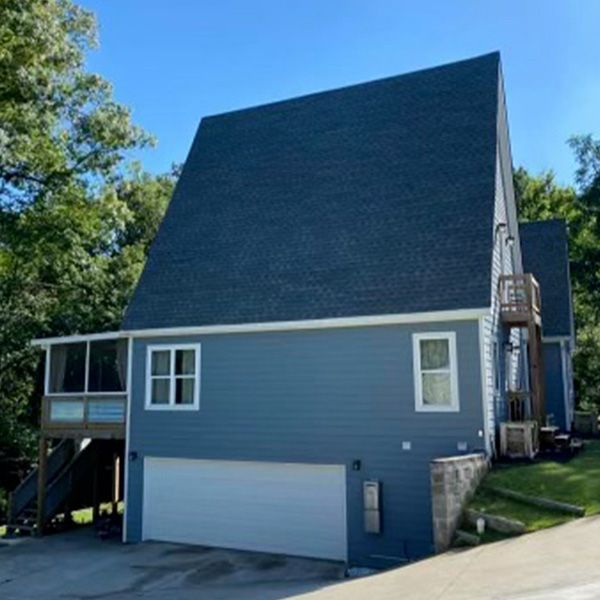 Blue house with steep roof, garage, and small side deck on a sunny day