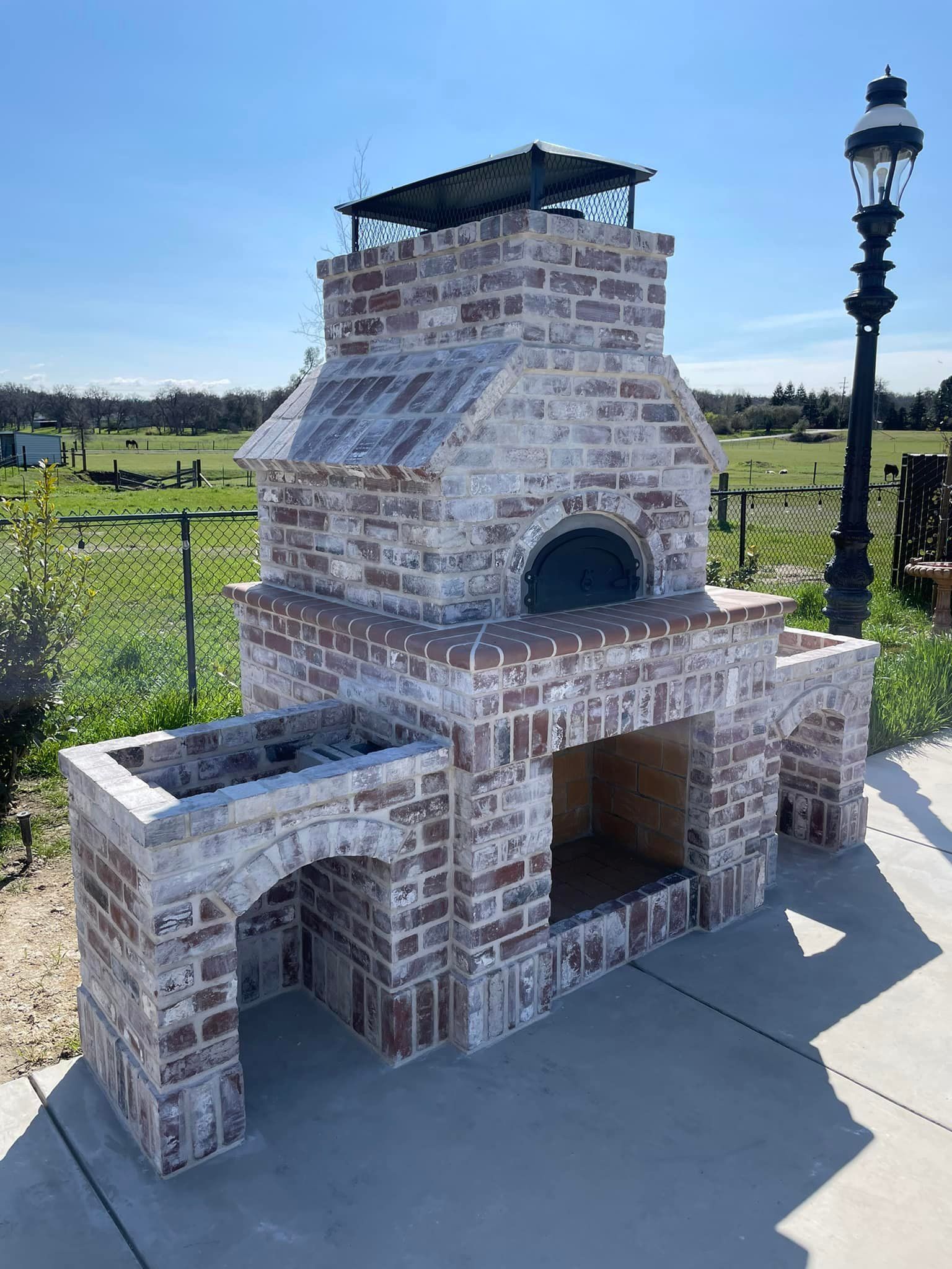 A large brick fireplace is sitting on a patio next to a field.