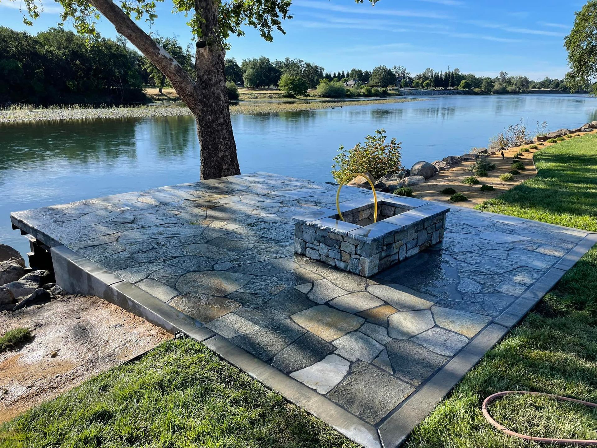 A stone patio with a fire pit next to a lake.